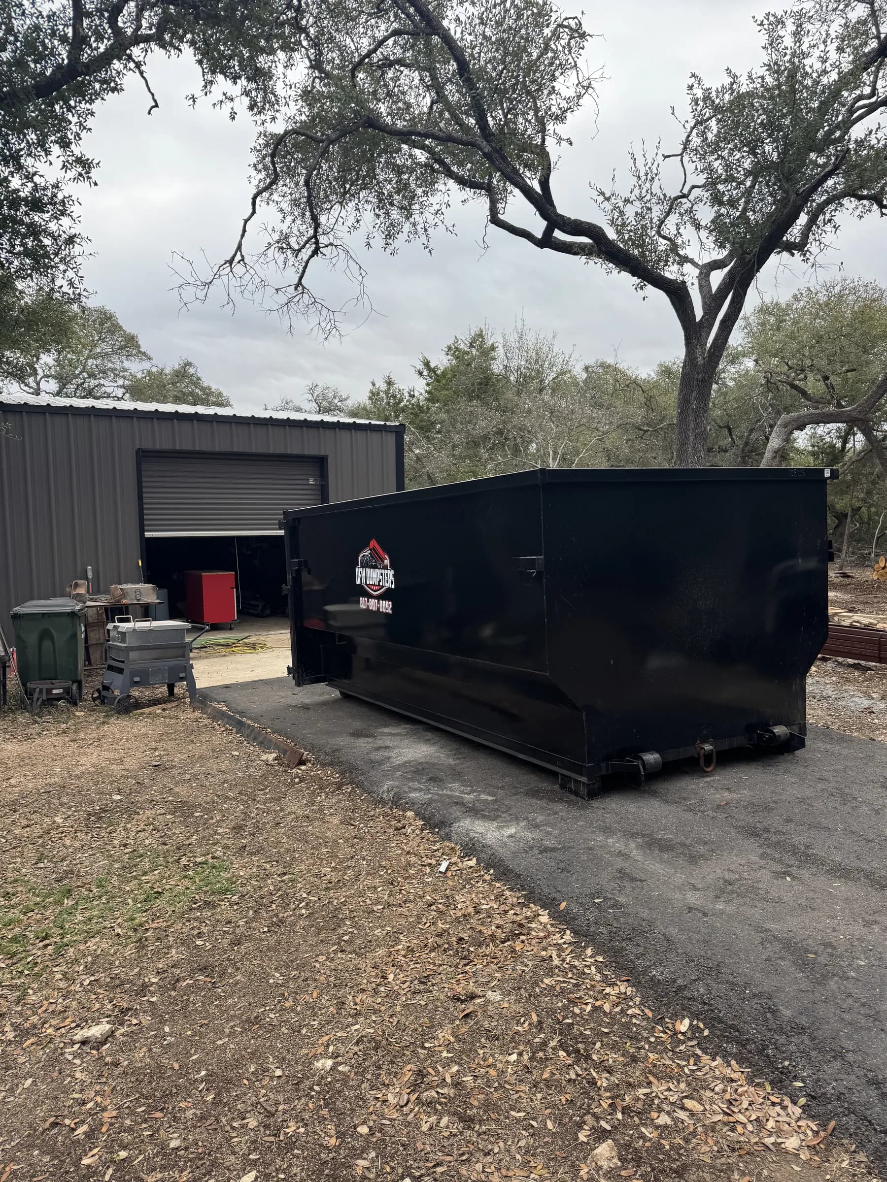 Large black RedLine dumpster on a concrete pad next to a metal warehouse
